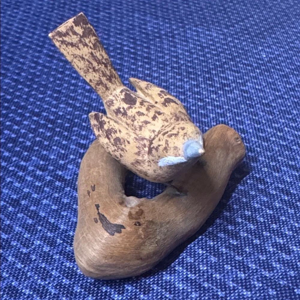 Hand carved wooden bird sculpture perched on a piece of natural wood signed